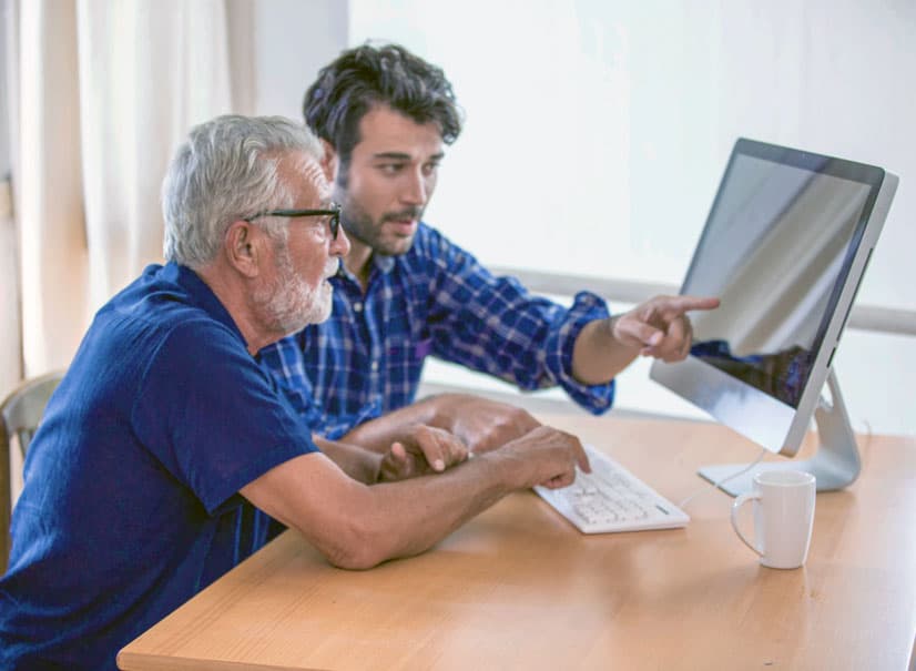 man helping senior man on all in one computer