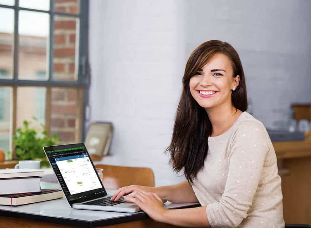 a smiling, young, female web designer sitting at a desk with a laptop.