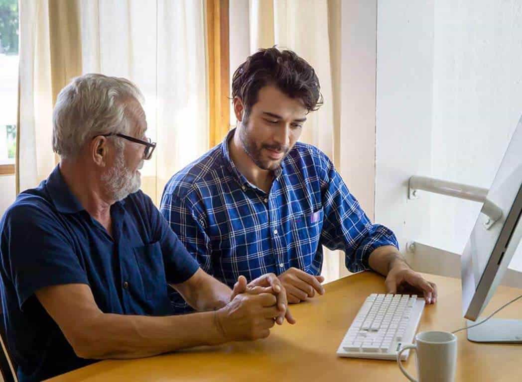 An in-home computer technician showing the homeowner, an older man, how to do something on his computer.
