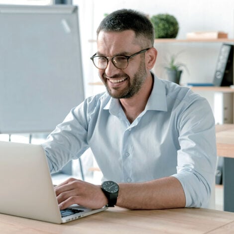 Smiling man on laptop at table in office