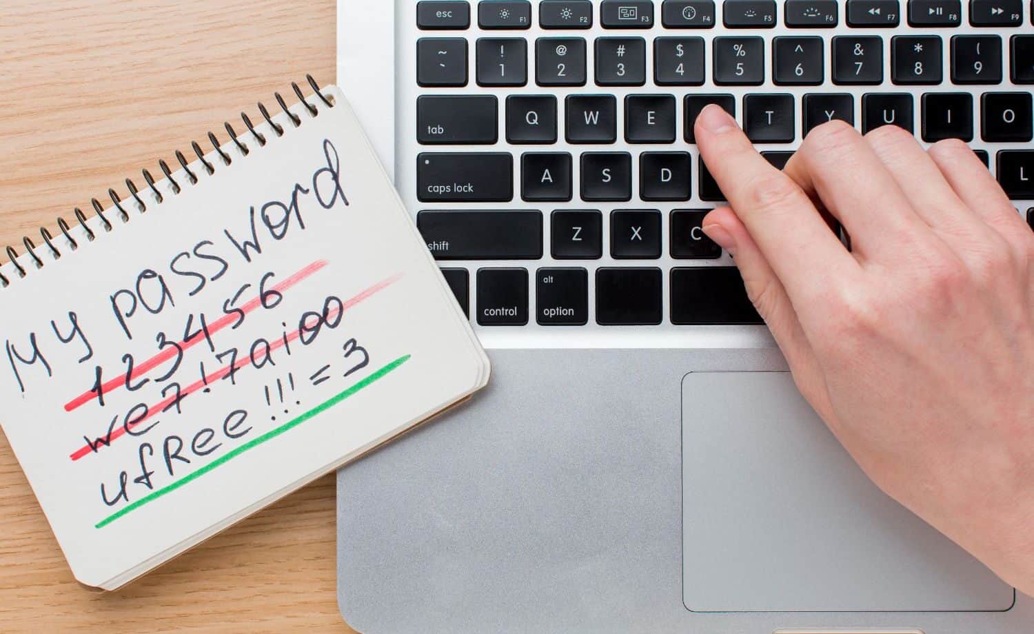 notebook with a bunch of handwritten passwords, some scratched out, next to a laptop.