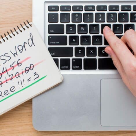 notebook with a bunch of handwritten passwords, some scratched out, next to a laptop.