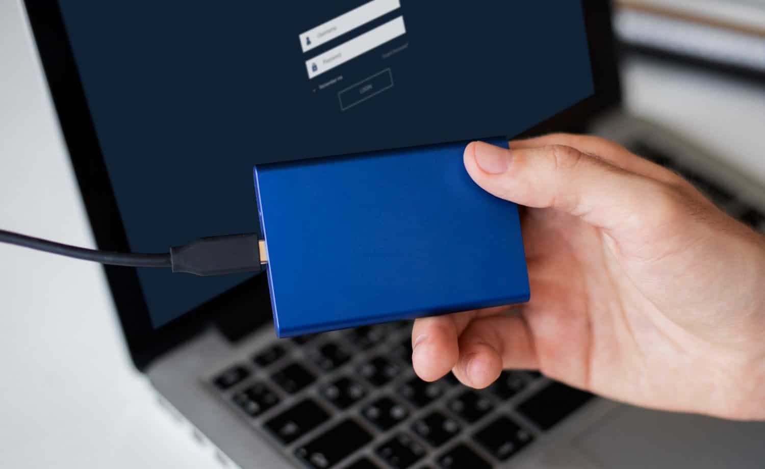 man holding a USB-C portable hard drive that's connected to his laptop.