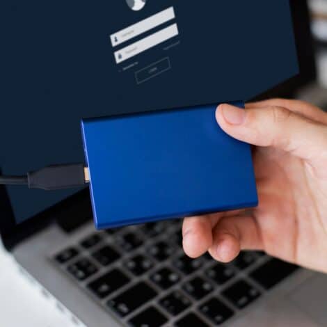 man holding a USB-C portable hard drive that's connected to his laptop.