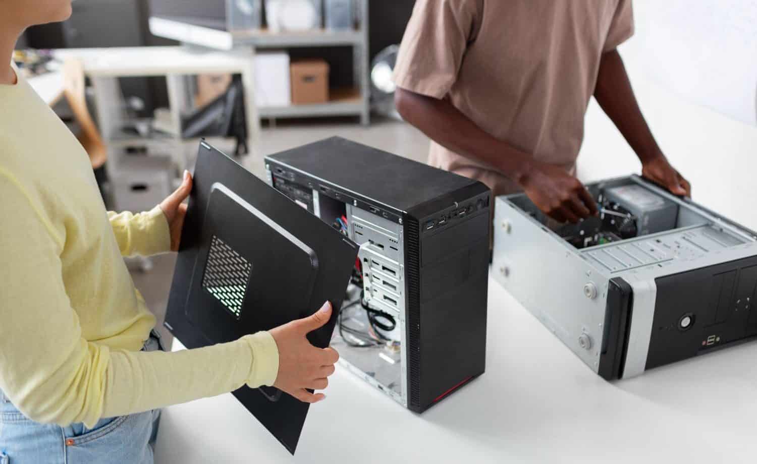 man and woman both independently working on cleaning the inside of 2 different desktop towers on a table