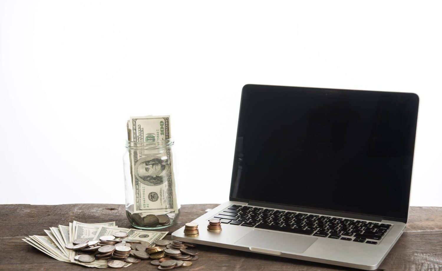 A laptop on a table next to a pile of cash - bills and loose change