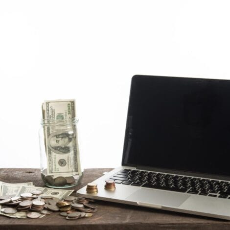 A laptop on a table next to a pile of cash - bills and loose change