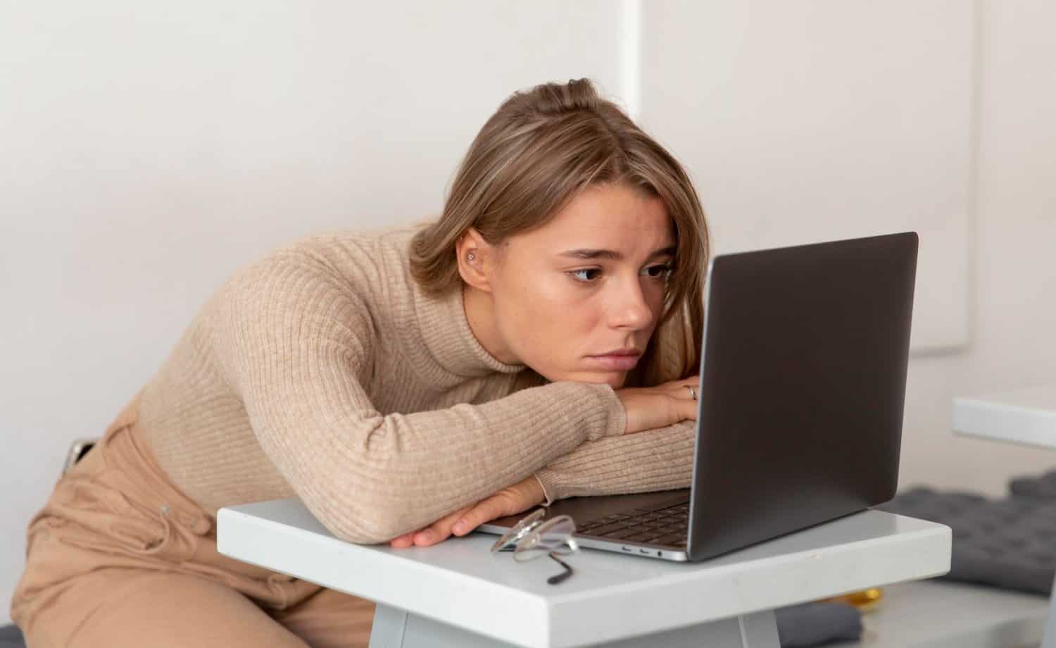 a defeated woman slumped at her desk over a slow computer