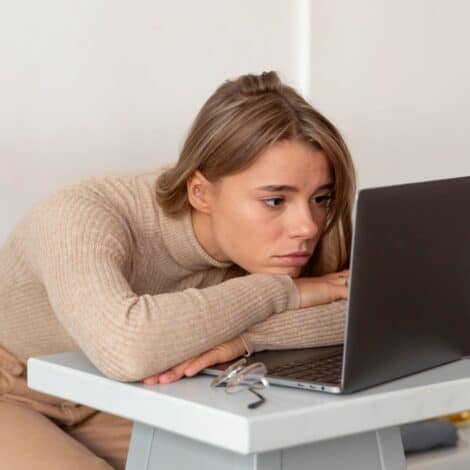 a defeated woman slumped at her desk over a slow computer