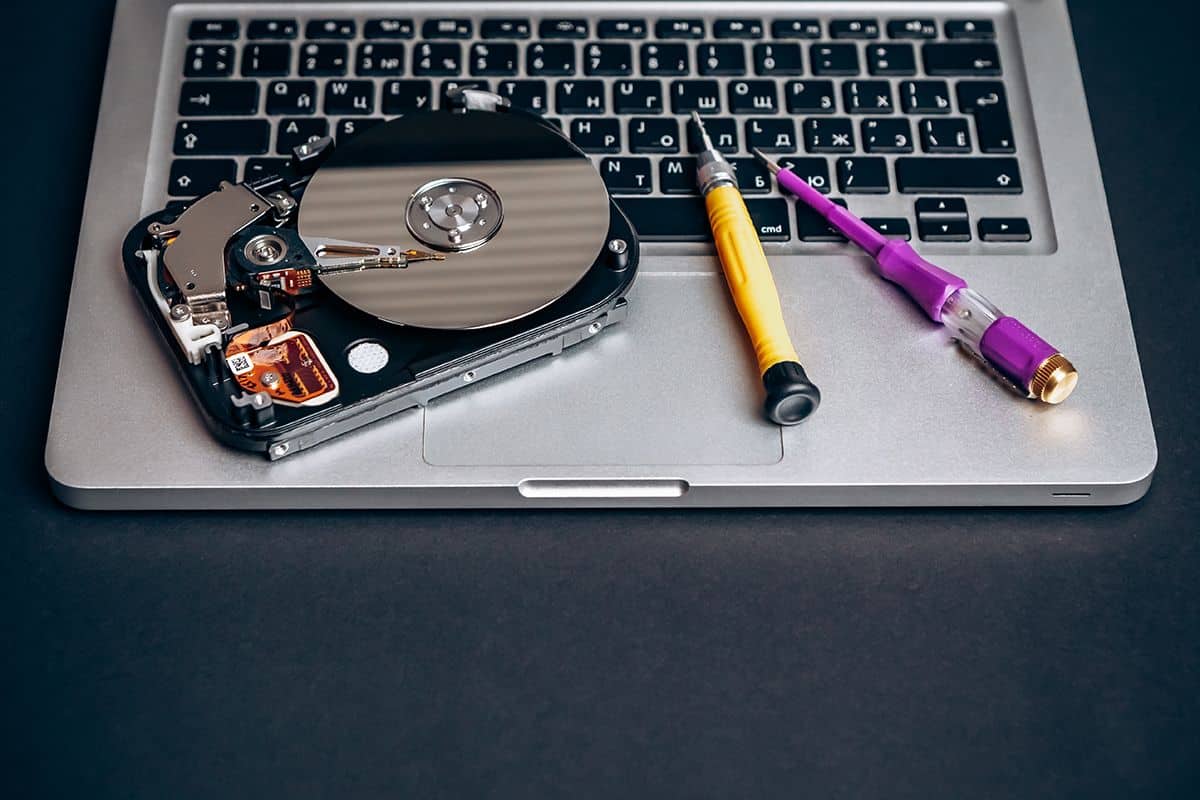 Open hard drive with exposed platters and tools placed on a laptop keyboard, illustrating a hard drive upgrade or repair service.