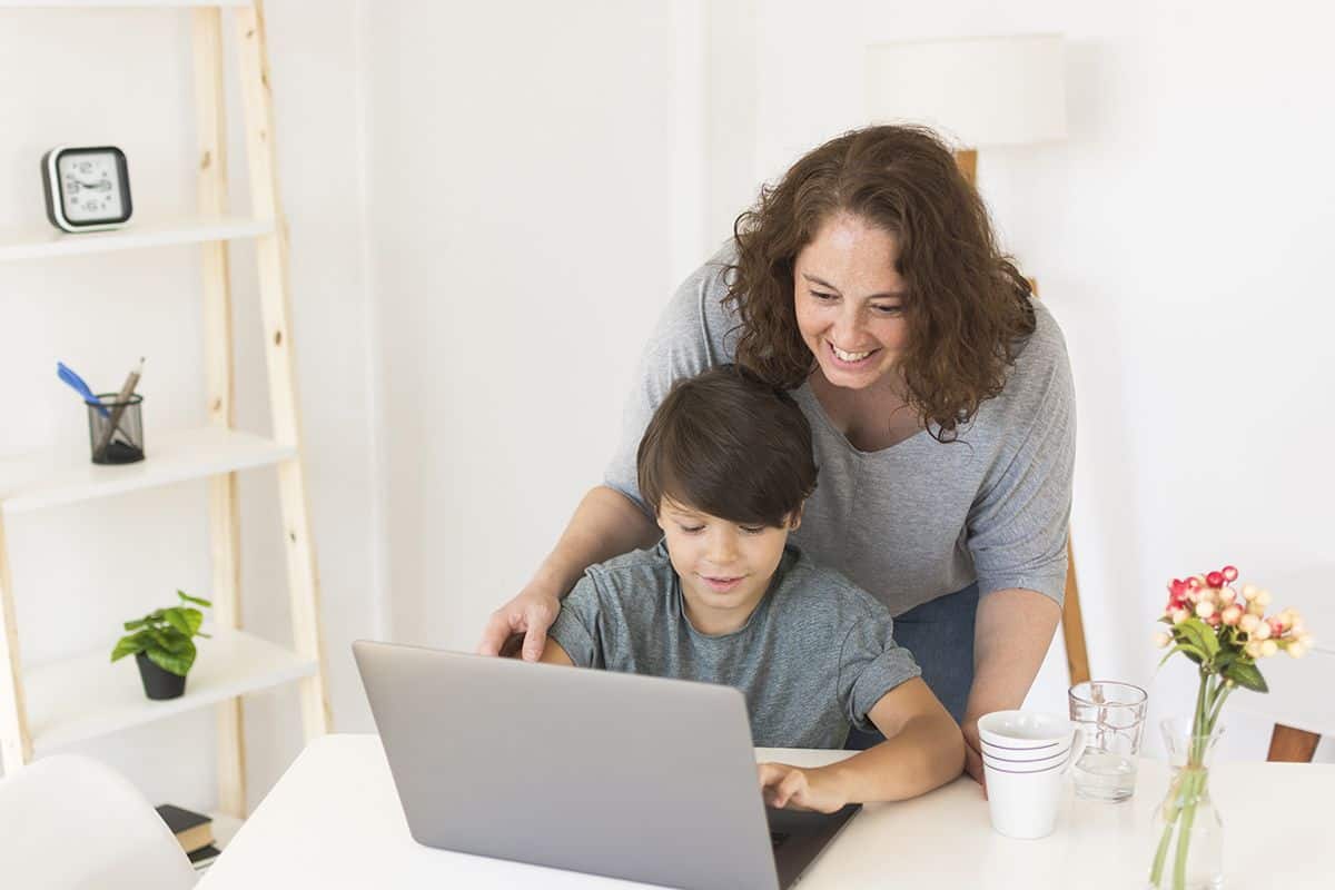 Smiling mother guiding her young child using a laptop, representing parental control setup and safe internet use.