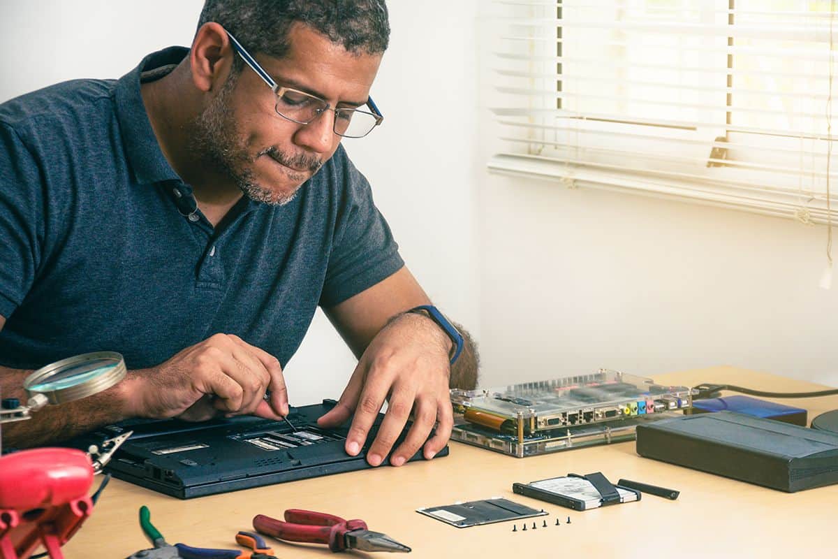 Technician upgrading a laptop's internal hardware at a workbench with tools and components, highlighting RAM upgrade or laptop memory replacement.